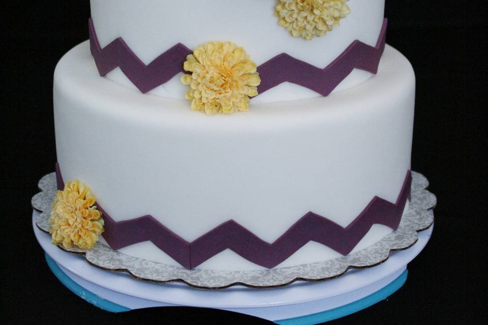 Fondant-covered cake with eggplant purple chevron pattern and silk flowers.