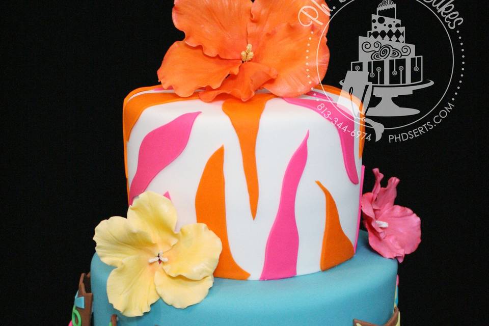 Hawaiian-themed luau cake with surf boards, tribal masks, a grass skirt, and tropical flowers