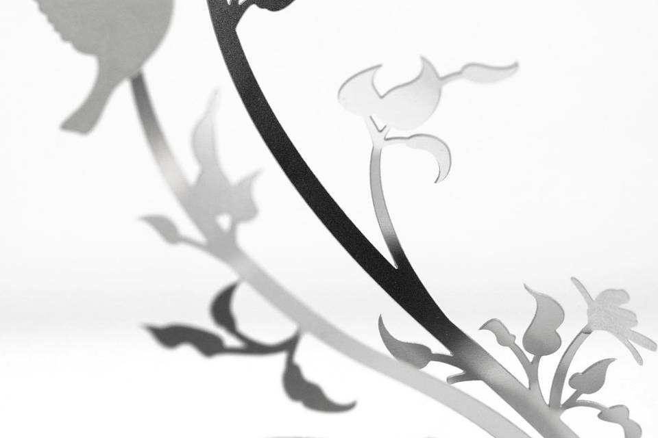The LOVE BIRDS metal invitation features two love birds swooping around floral vines creating a romantic invitation. Mails flat and is folded into a sculpture by guests. Folding at the perforations will allow the vines to stand and be sculpted – each sculpture will be as unique as your guests. Place a tea light behind the sculpture for beautiful, dancing shadows. Or use as home décor. LOVE BIRDS is also available as a favor with slits into which an escort card can be inserted.
