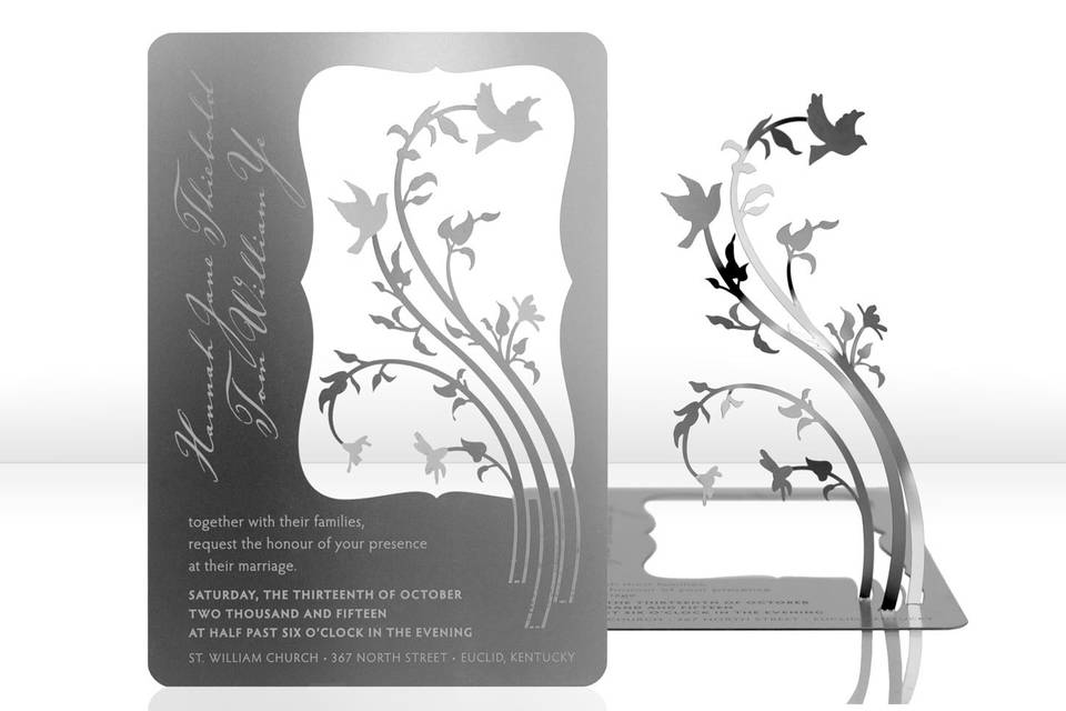 The LOVE BIRDS metal invitation features two love birds swooping around floral vines creating a romantic invitation. Mails flat and is folded into a sculpture by guests. Folding at the perforations will allow the vines to stand and be sculpted – each sculpture will be as unique as your guests. Place a tea light behind the sculpture for beautiful, dancing shadows. Or use as home décor. LOVE BIRDS is also available as a favor with slits into which an escort card can be inserted.