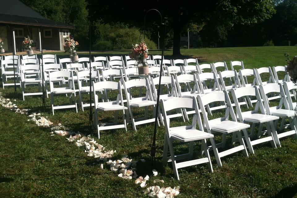 Outdoor vintage barn wedding in blush peach and creamy ivory tones with roses, stock and baby's breath in mason jars adorned with burlap and lace ribbon hanging from shepards hooks.