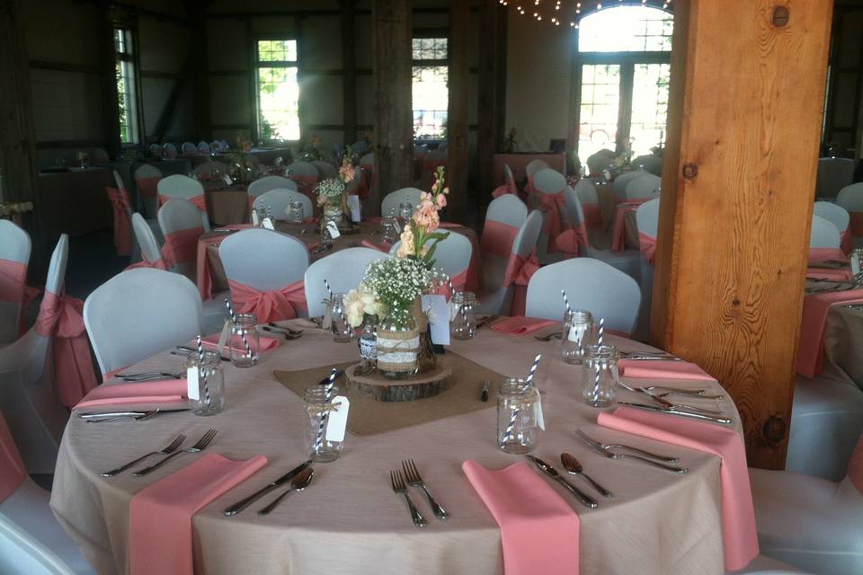 Vintage barn wedding in blush peach and creamy ivory tones with roses, stock and baby's breath in various size jars adorned with burlap, twine and lace nestled on a rustic wooden slice.