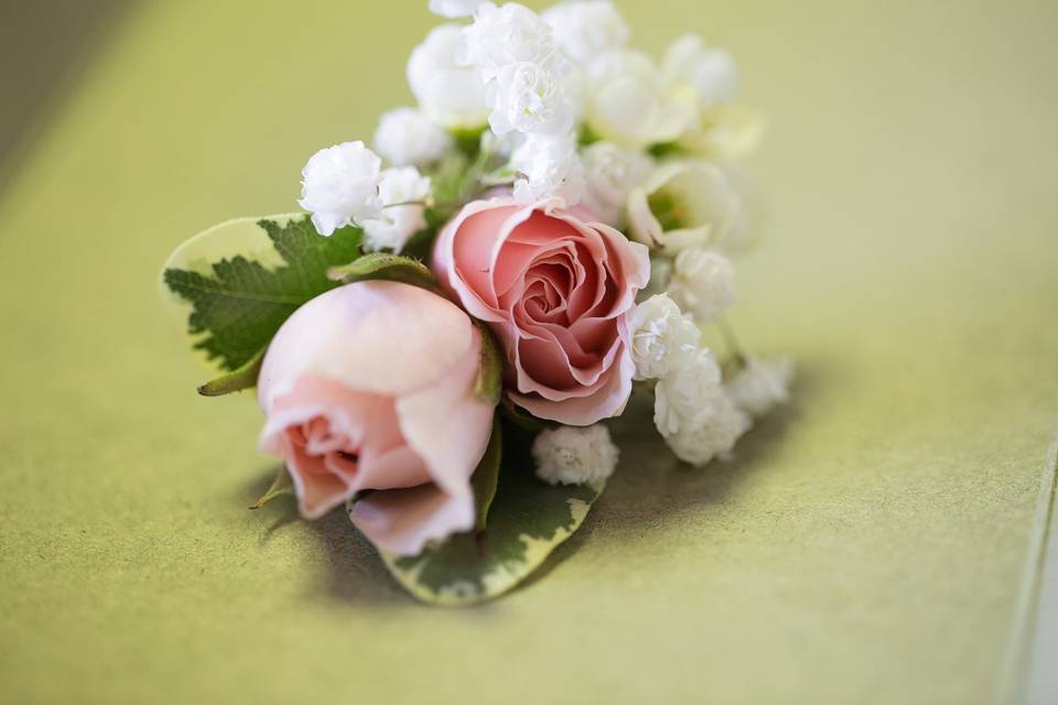 Boutonniere in soft pink with spray roses, wax flower and baby's breath wrapped with twine.