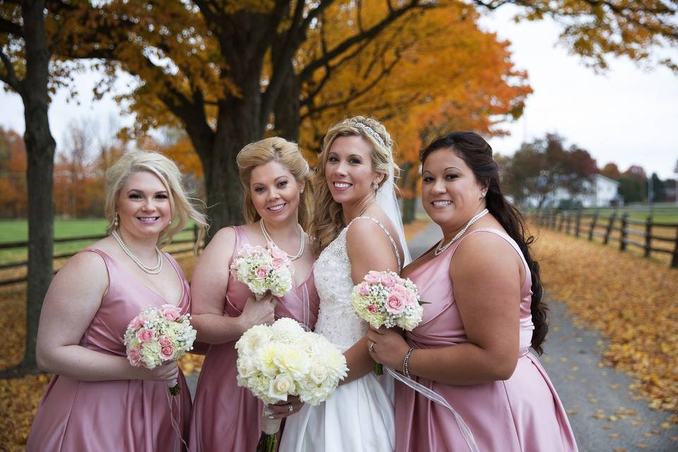 Bride with bridesmaids in autumn outdoor scene with bouquets in creams and soft pinks with roses, hydrangeas, spray roses, dahlias, wax flower and baby's breath.