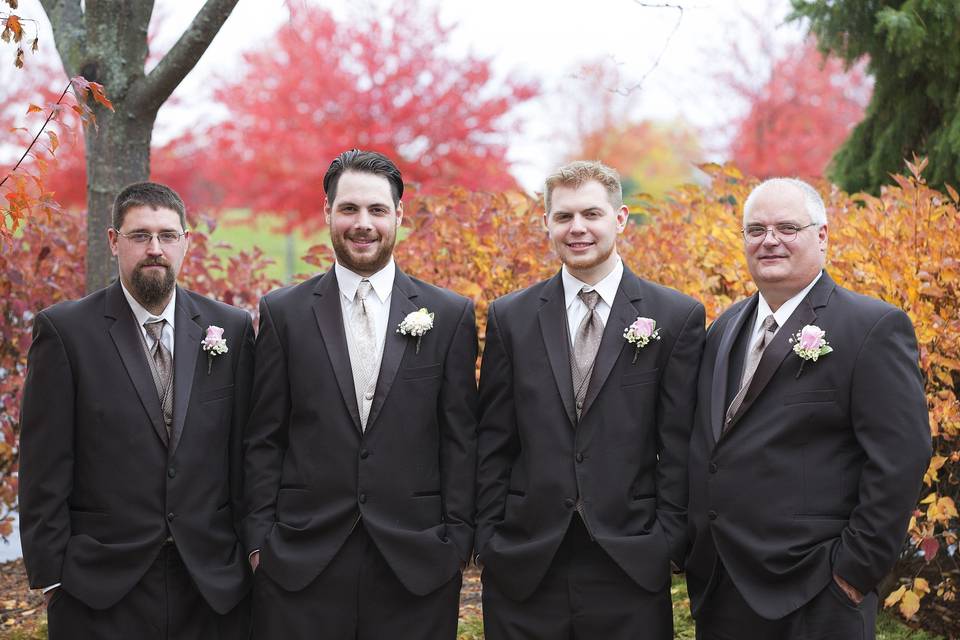 Groom with groomsmen in autumn outdoor setting with boutonnieres in soft pink roses with wax flower and baby's breath wrapped in twine.