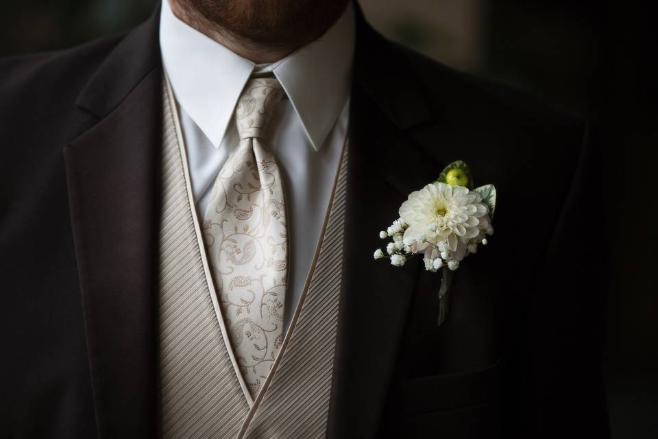 Groom with boutonniere of creamy dahlia with baby's breath wrapped in twine.