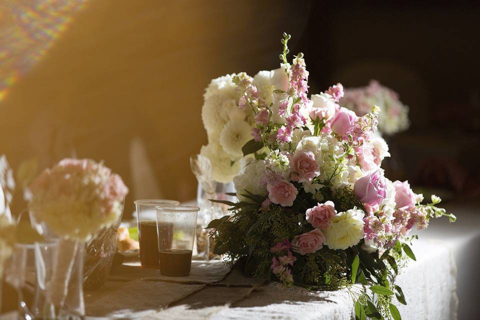 Reception flowers for bridal table centerpiece in soft creams and pinks with larkspur, hydrangeas, roses, spray rose and dahlias, overflowing with seeded eucalyptus.