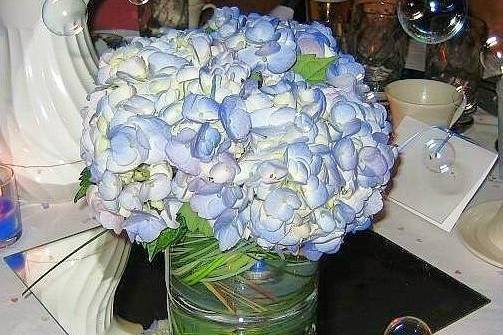 Reception Centerpiece for Guest Table: stunning blue hydrangeas in a low glass cylinder lined with bear and lily grasses with a submerged blue light in the bottom.