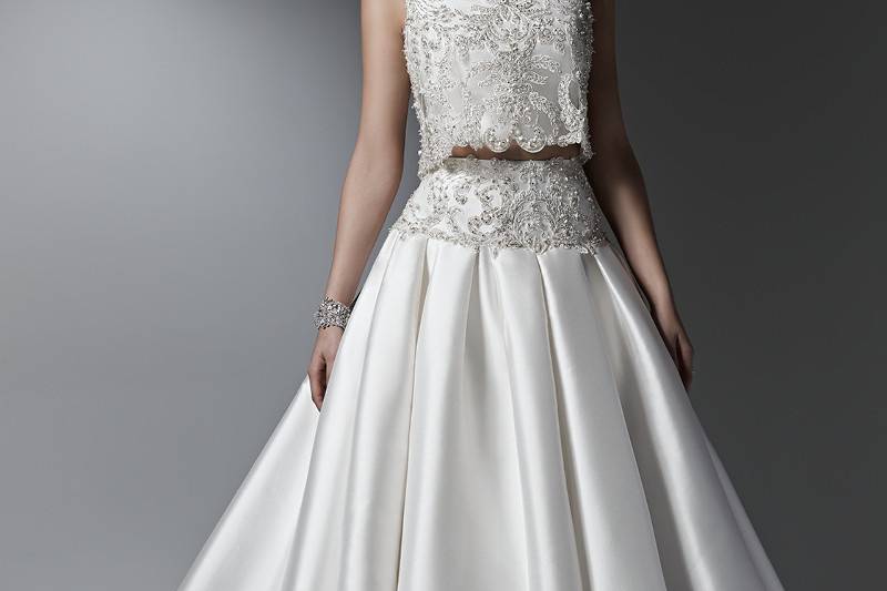 Style Dharma <br> Luxurious and utterly breathtaking, this two-piece ball gown wedding dress is the epitome of glamour with a voluminous Vizela Mikado skirt with side seam pockets and a cropped, bead encrusted, lace top with Swarovski crystals. Finished with bateau neckline and zipper closure.