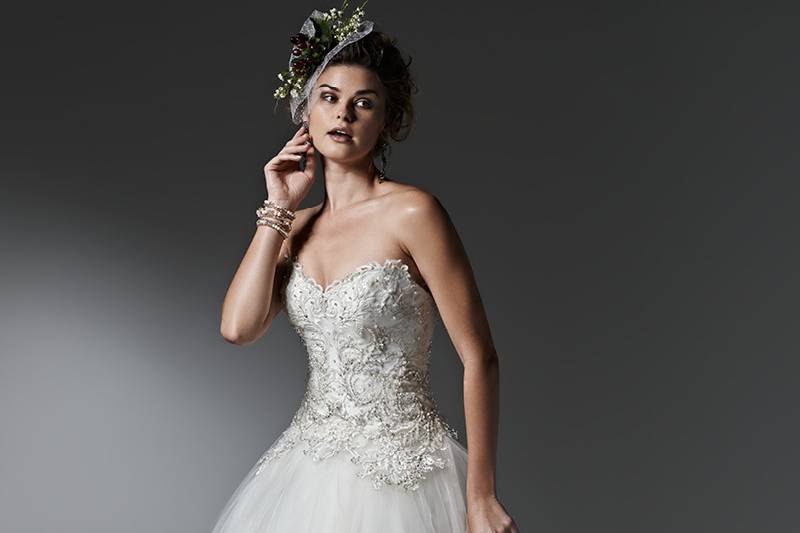 Style Sigourney<br> Layers of lightweight tulle create the gorgeous skirt of this whimsical ball gown, featuring a lace and Swarovski crystal studded bodice. Finished with sweetheart neckline and pearl buttons over zipper closure.