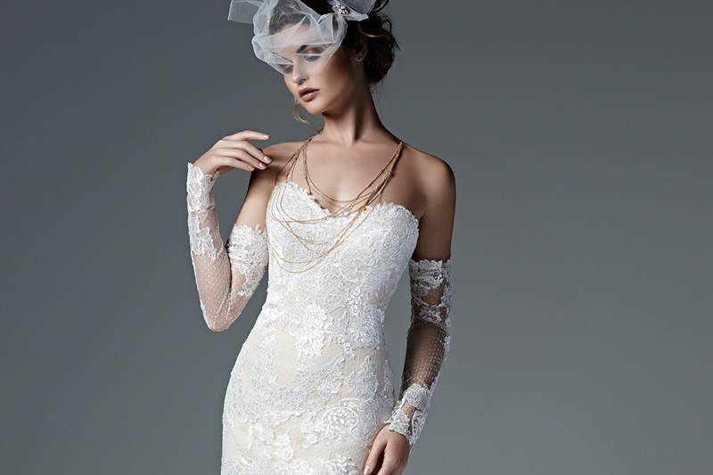 Style Alexandra <br> Stunning embroidered lace and delicate dotted tulle combine to create this chic sheath wedding dress with scoop neckline and dramatic illusion lace gauntlets. Finished with inner corset and pearl buttons over zipper closure.