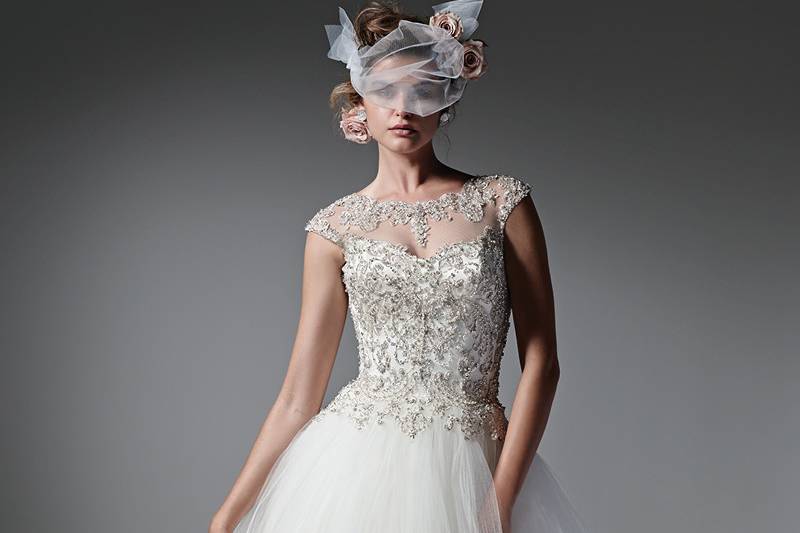 Style Monaco <br> Modern and romantic, this pleated tulle and Chic organza ball gown sparkles with a Swarovski crystal encrusted bodice. A demure illusion neckline, back, and cap-sleeves are sprinkled with glittering crystals. Finished with crystal buttons over zipper closure.