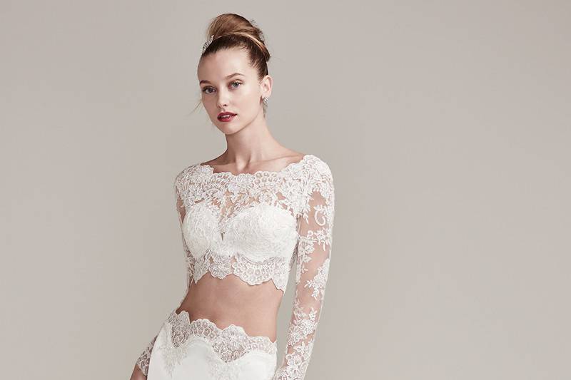 Fiona<br> An illusion lace crop top is accented with a stunning scalloped lace bateau neckline and long sleeves. The matching Belize satin sheath skirt with lace trim creates a fashion-forward two-piece wedding dress style.   Complete with a detailed illusion lace trimmed train and ruching. Finished with covered buttons and zipper closure.