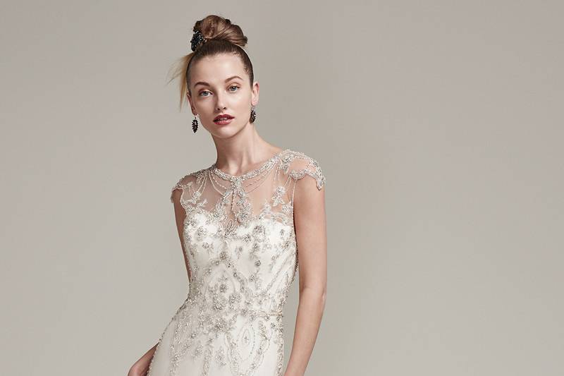 Syanne <br> Eye-catching beading adorns the sleek silhouette of this tulle sheath wedding dress, featuring an artistically embellished illusion neckline and cap-sleeves. Complete with stunning beaded illusion keyhole back. Finished with crystal buttons over zipper closure.