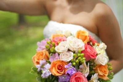 A beautiful summer bride carrying coral and ivory roses, stock, alstroemeria in a hand tied summer bouquet