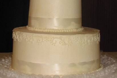 Embroidery and Ribbon Wedding CakeTwo tier wedding cake topped with Fresh Rose bouquet. Cake is iced in wedding buttercream and each tier is wrapped with Ivory ribbon. There is a decorative band of embroidery piped around the top of each tier.