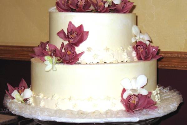 Small wedding cake wrapped with an edible band of fondant lace and adorned with fresh orchids