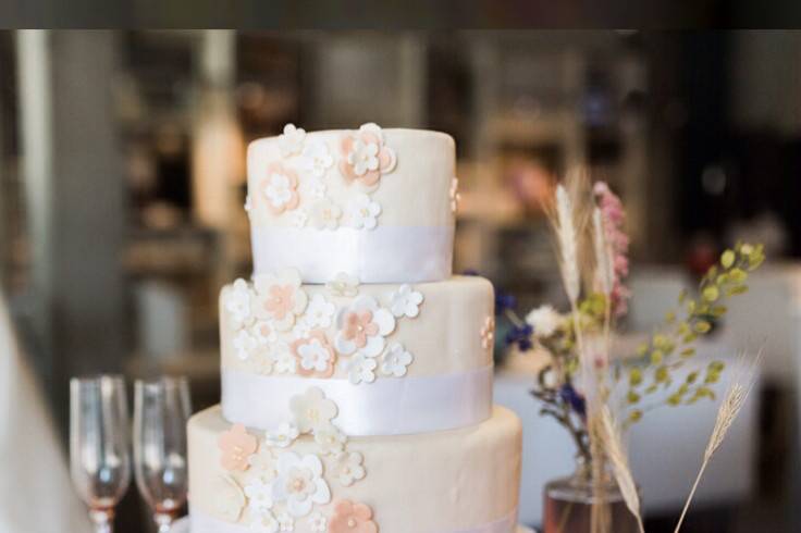 A 3 tier Nashville wedding cake covered in peach fondant blossom flowers surrounded in white ribbon