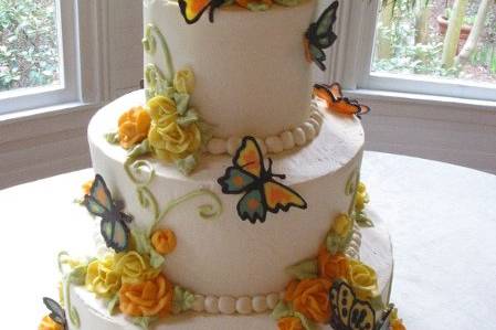 White chocolate butterflies flutter around buttercream roses on an ivory buttercream frosted cake.