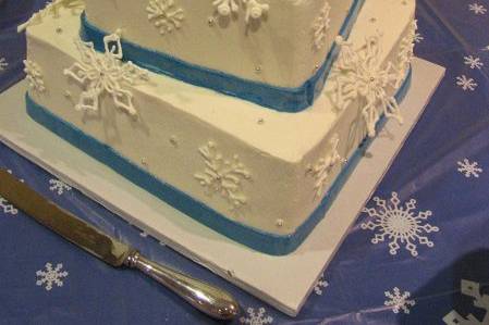 Royal icing snowflakes and blue fondant ribbon adorn a cool white buttercream-frosted cake.