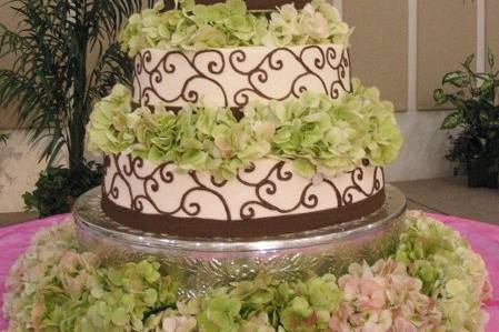 A four tier buttercream cake featuring a monogram top, fresh hydrangeas, and a replicated scrollwork design created by the bride's sister.